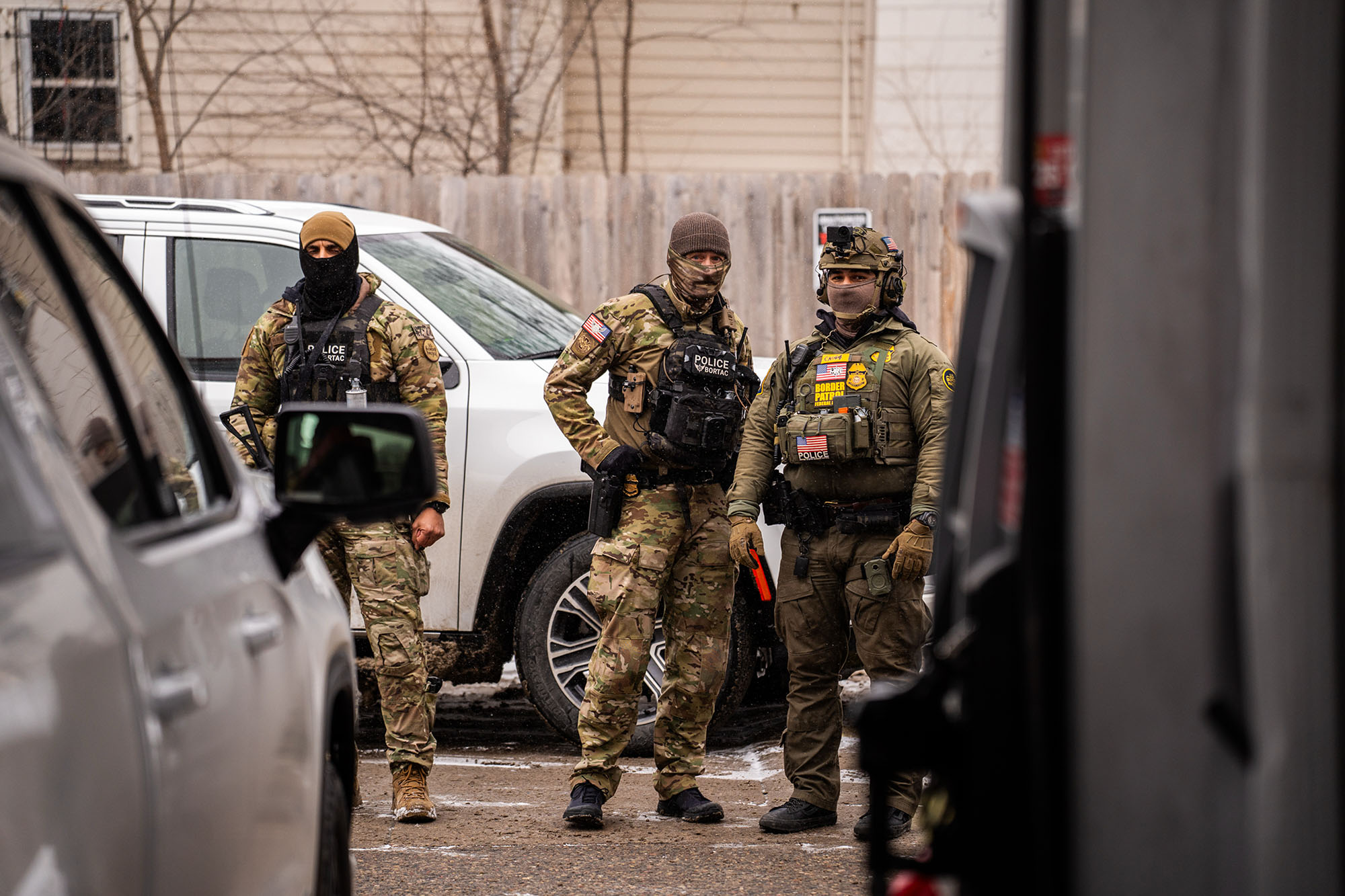 Group of three federal agents standing behind cars.
