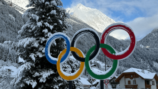 The olympic rings covered in snow next to a snowy mountainside.