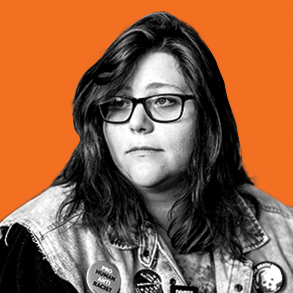 Heavier set young woman wearing a hoodie, glasses, and a decorated denim vest looks away from the camera. 