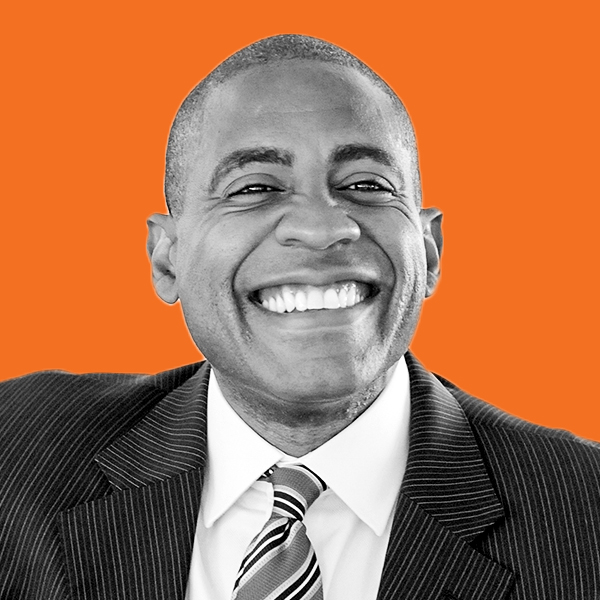 An African American man in a suit and tie grinning widely. 