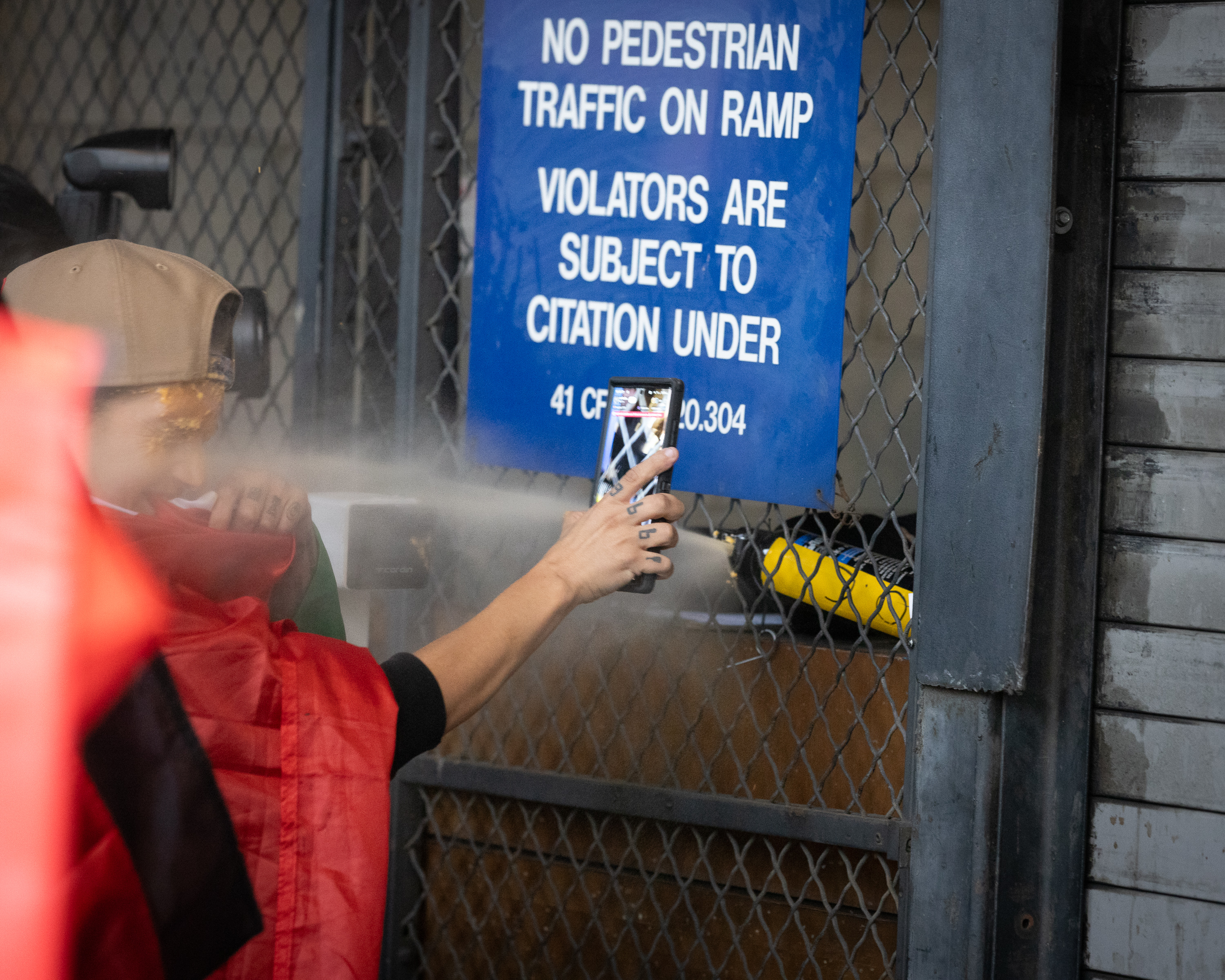 A person holding a cellphone is pepper sprayed in the face through a gated door.