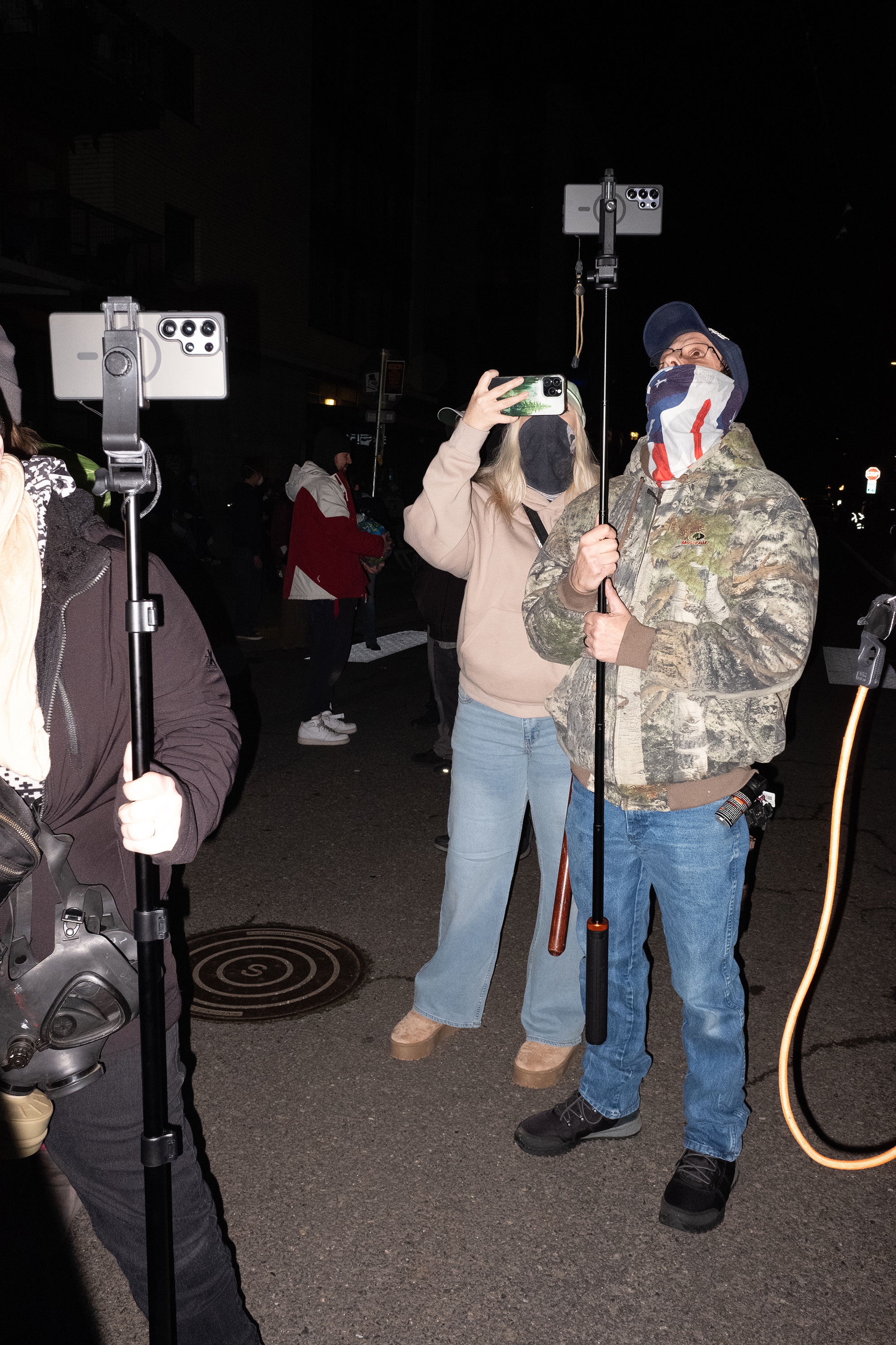 Three people with cellphones, two of them on long poles.