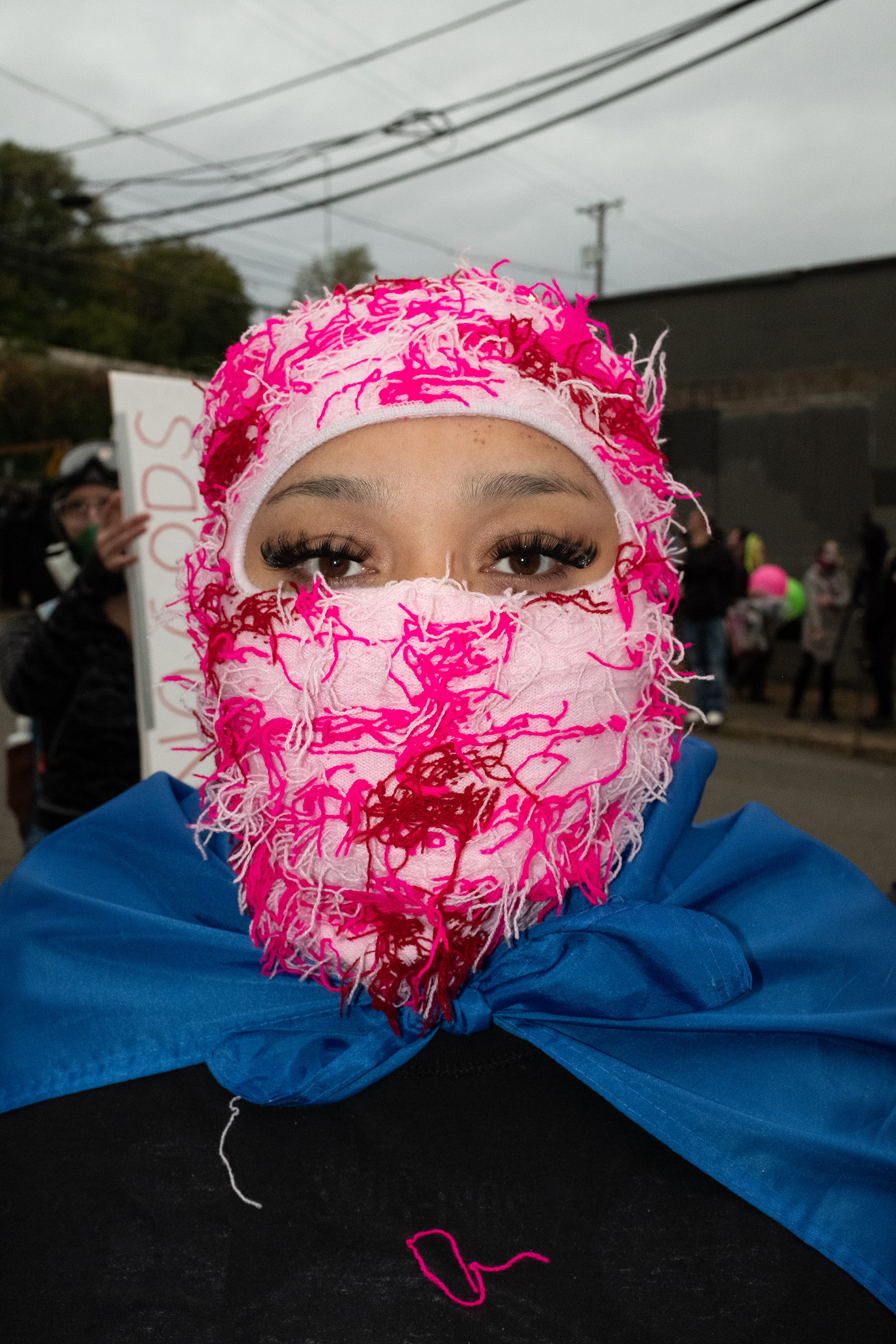 Woman wearing a blue cape with a red and pink scarf wrapped around her face.