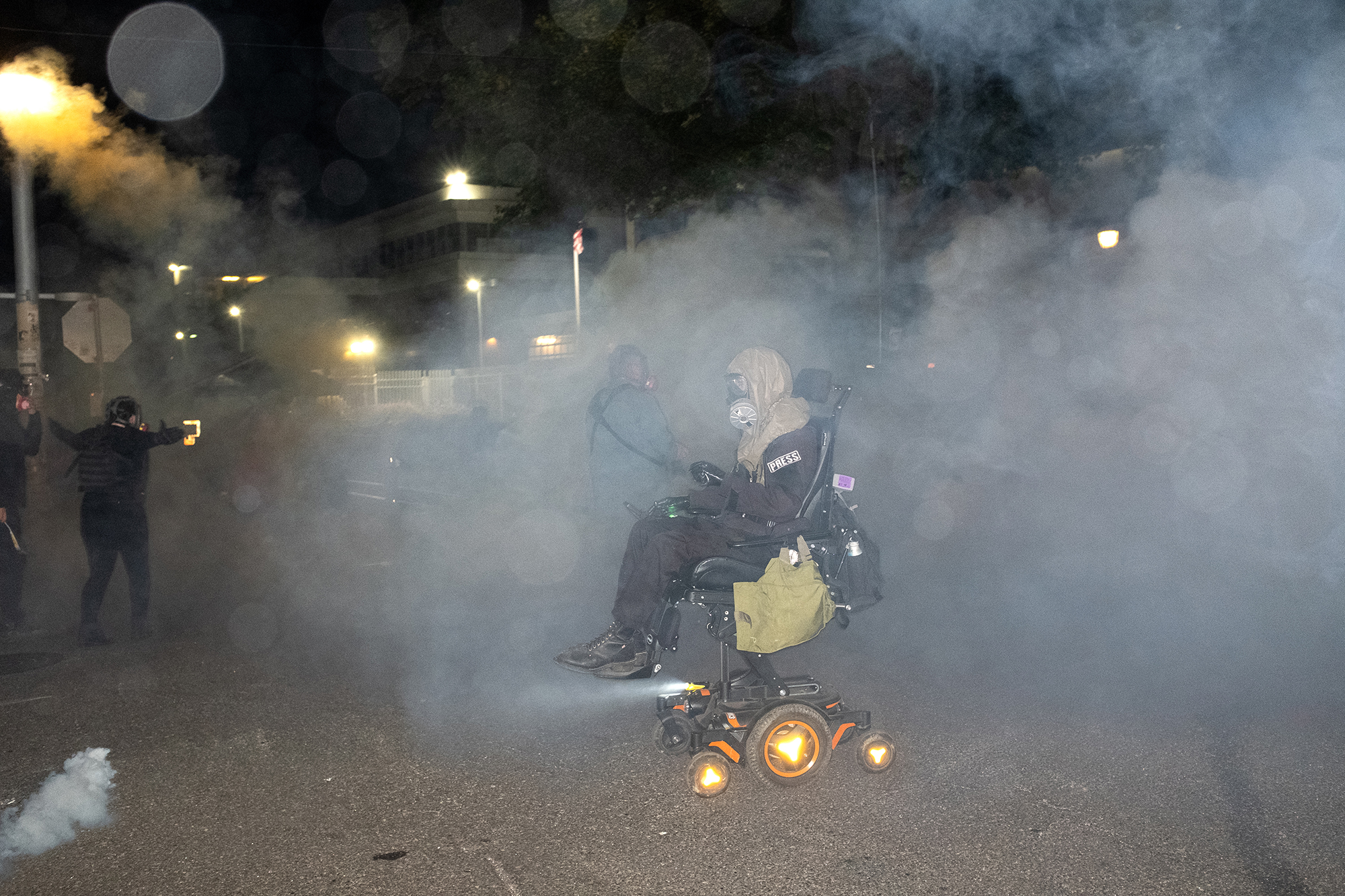 Person in a wheelchair moves through a cloud of smoke at night.