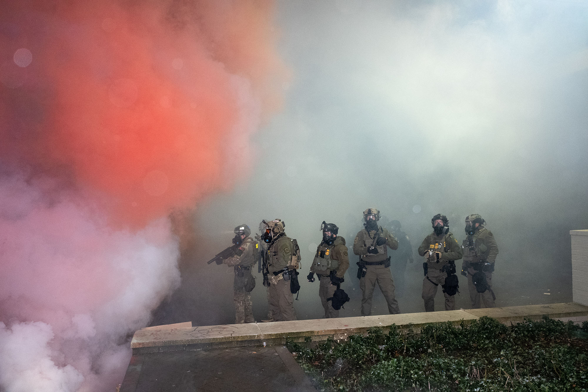 Line of heavily armored agents walk through clouds of gas.