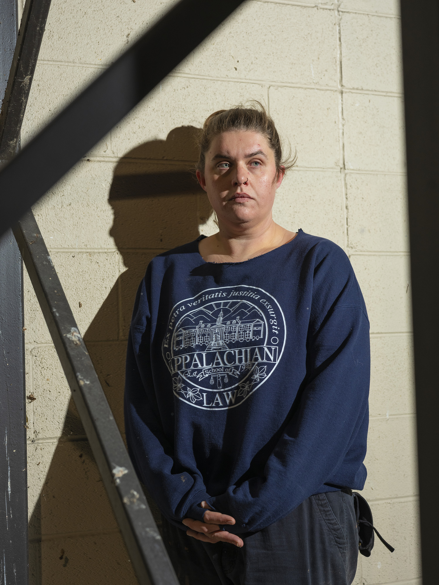 A woman with dark blond hair pulled back, standing against a cinder-block wall wearing an Appalachian Law sweatshirt.