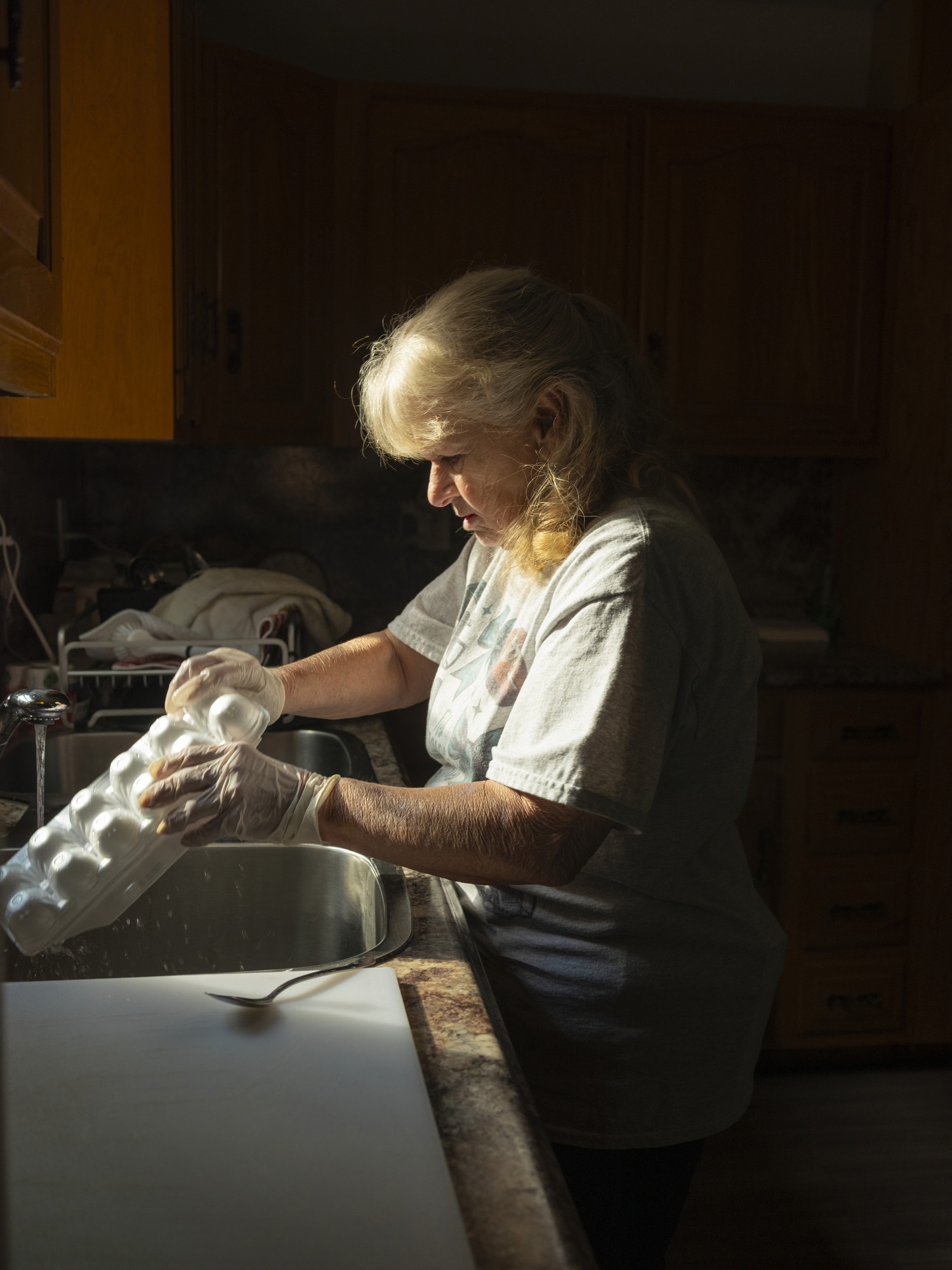 A woman stands at a sink rinsing a styrofoam egg carton.