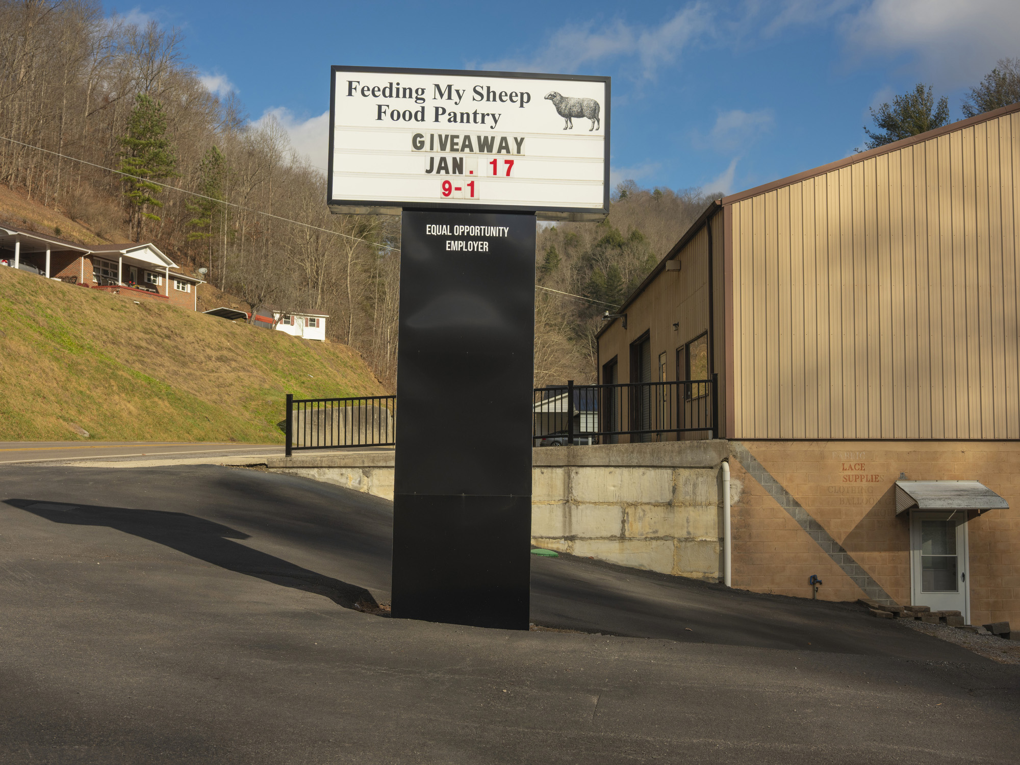 Outside a warehouse, a sign reads, "Feeding My Sheep Food Pantry; Giveaway Jan. 17, 9-1."