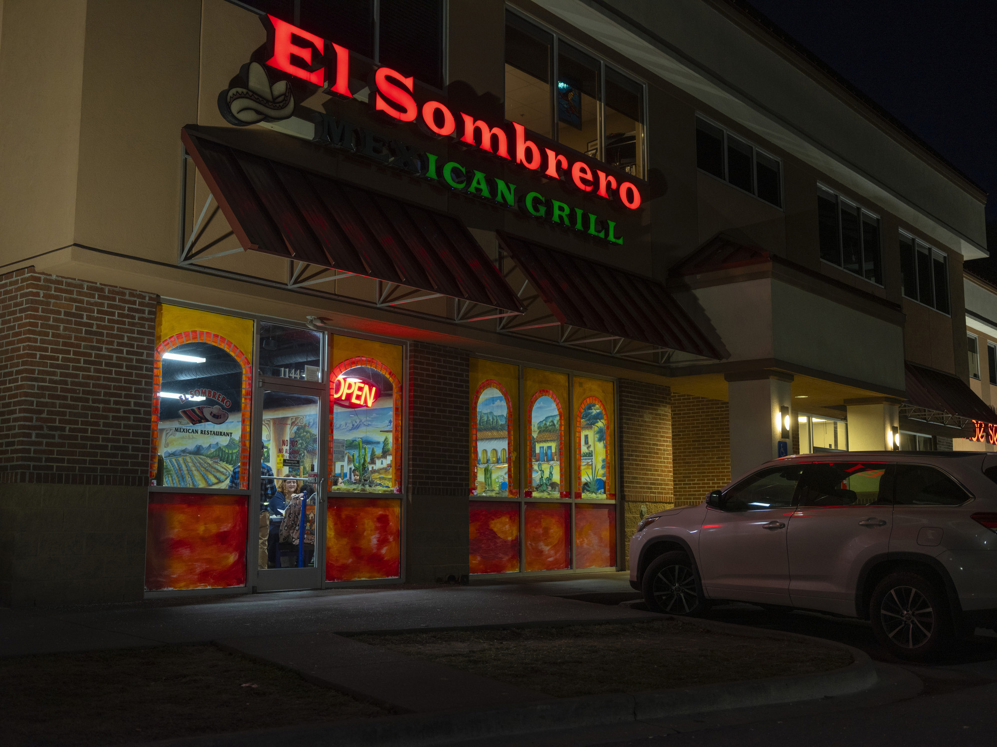 The exterior of a Mexican restaurant with one car parked out front, seen at night. The lit-up sign reads, "El Sombrero Mexican Grill."
