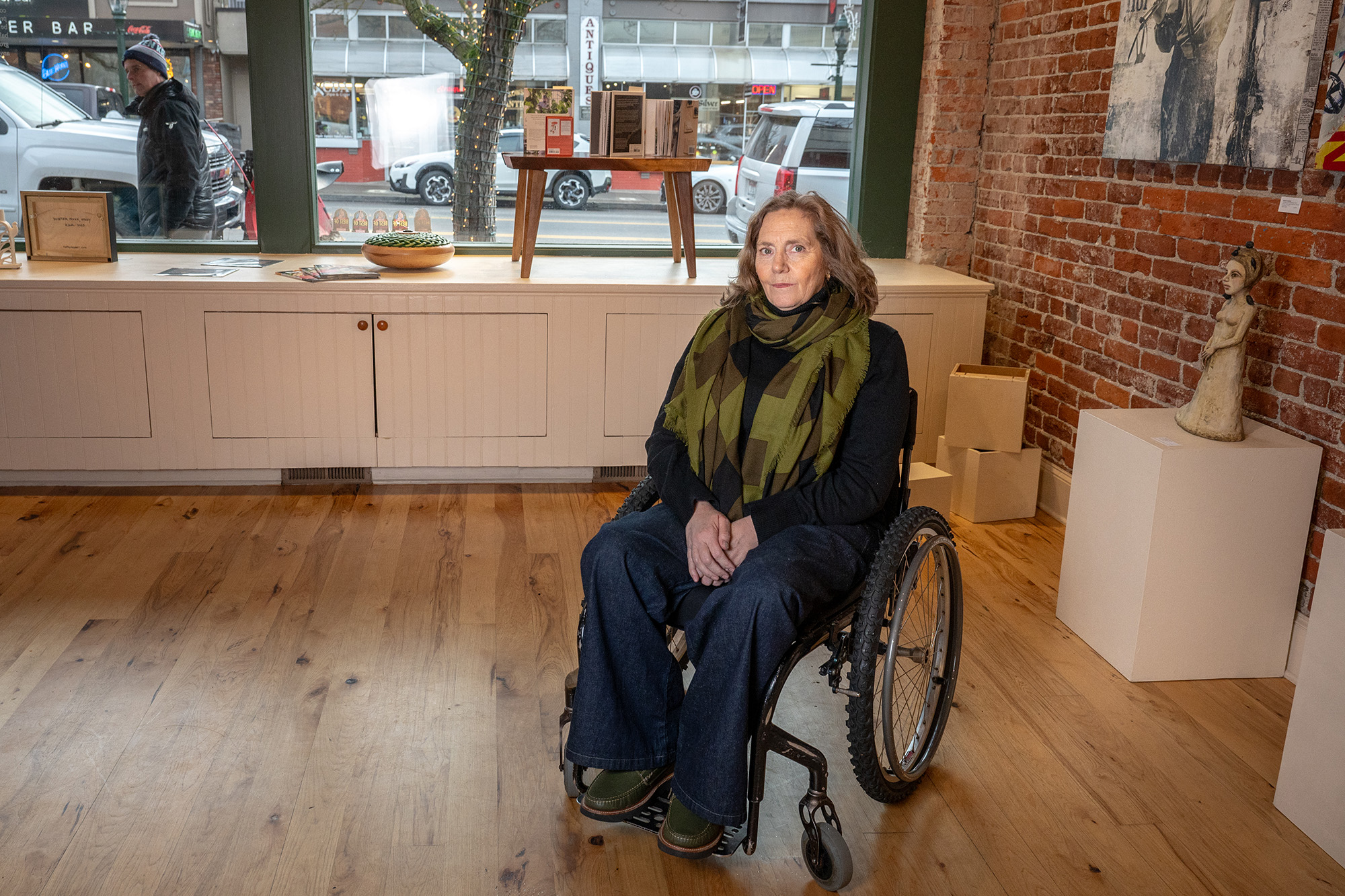 A middle aged woman in a wheelchair, poses for a portrait in the middle of an art gallery.