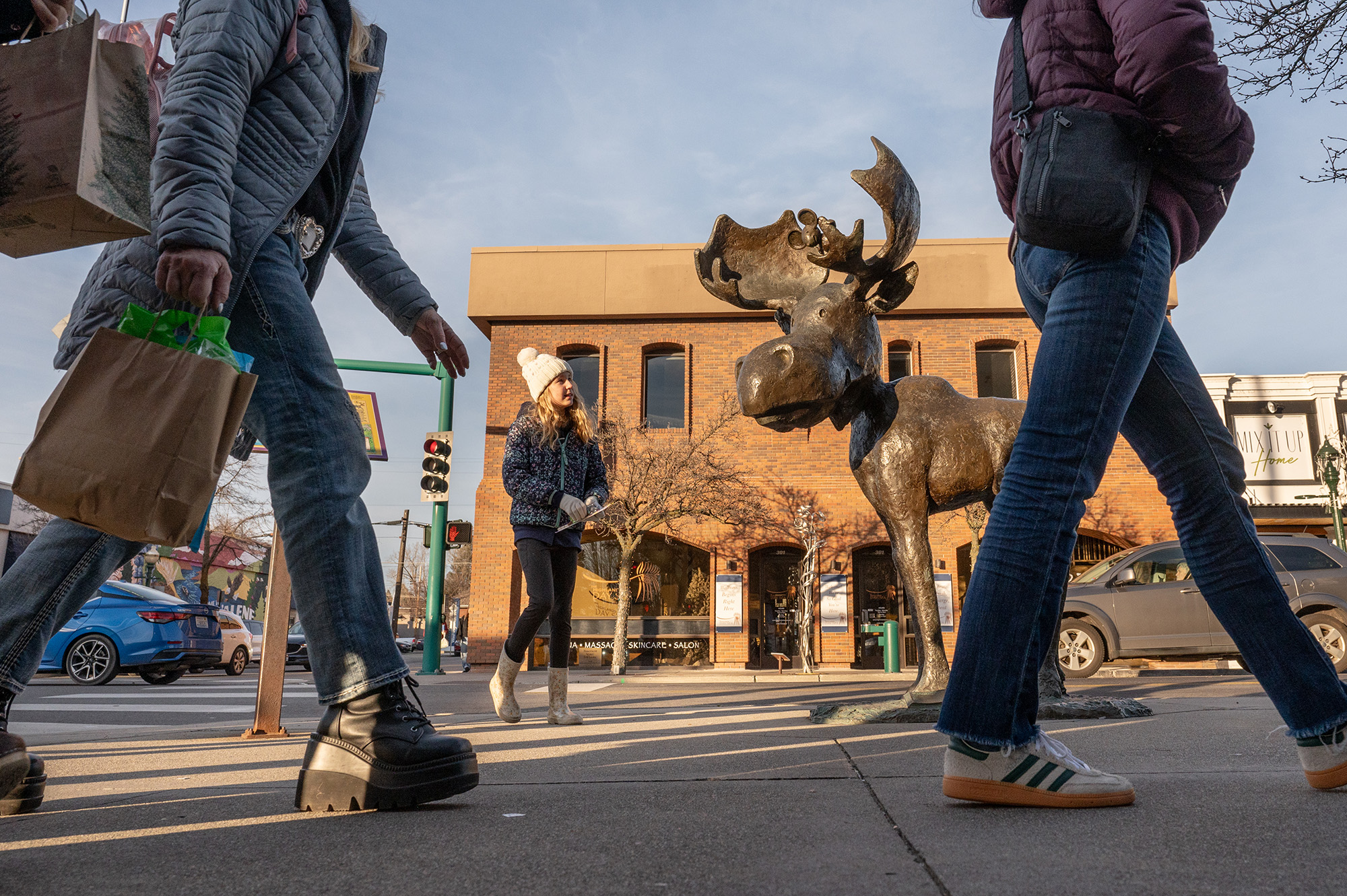Low-angle view of a statue of a moose in a downtown as people walk by and a child admires the statue.
