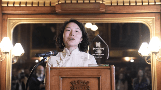 An Asian woman stands in front of a lectern.