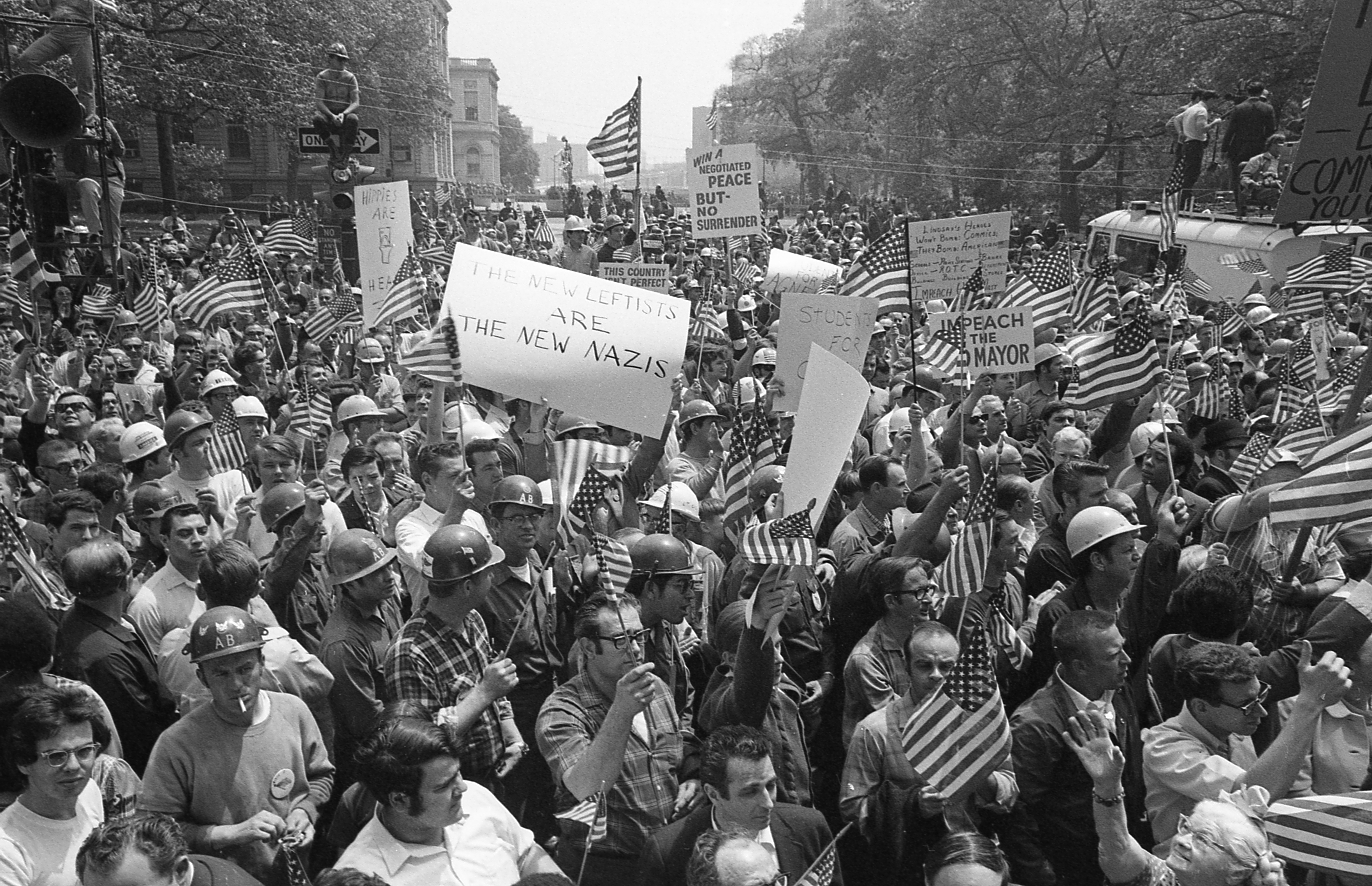 Large group of protesters, many wearing hard hats and waving American flags.