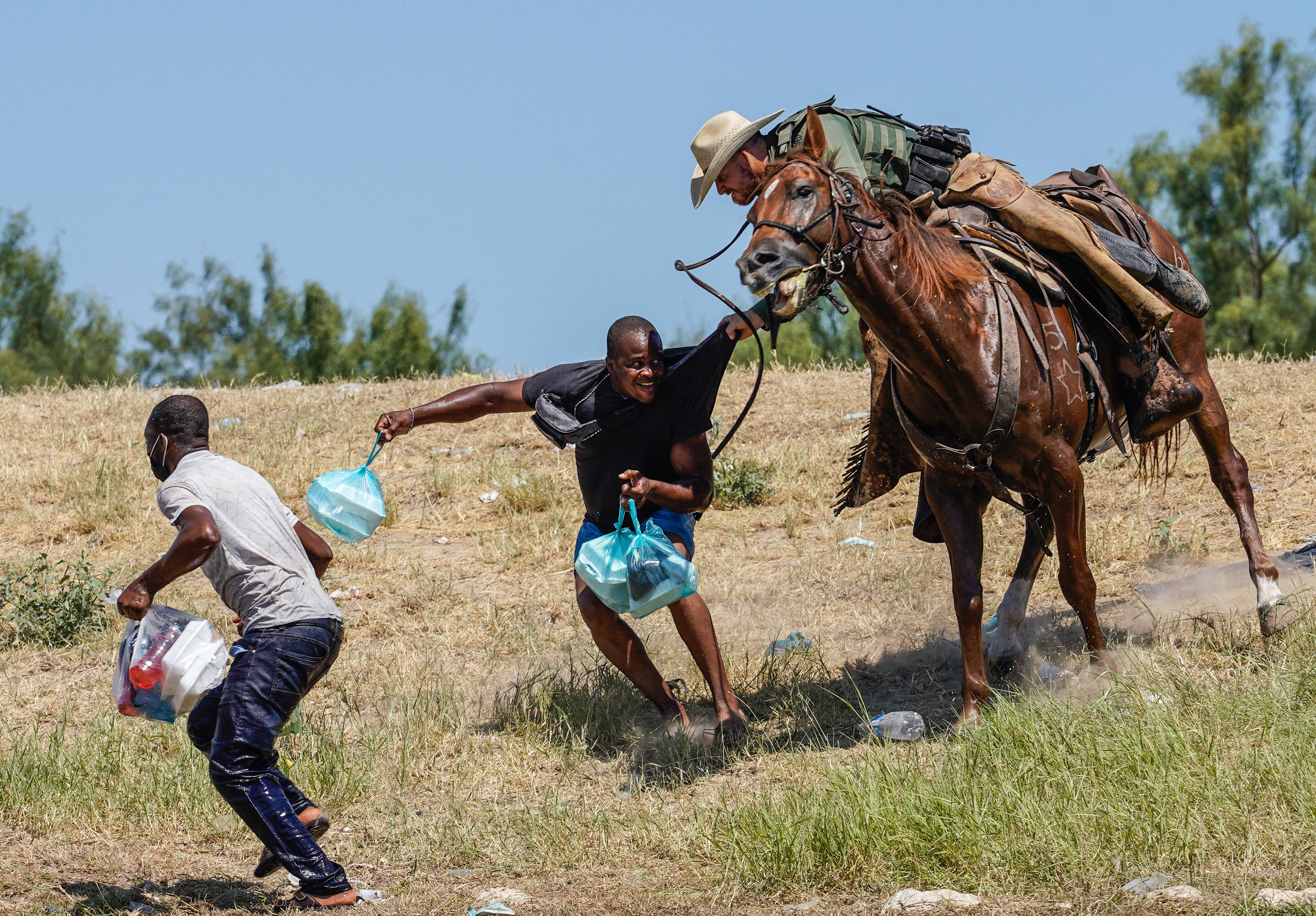 A border patrol agent on horseback grabs a haitian migrant as he's trying to run away.