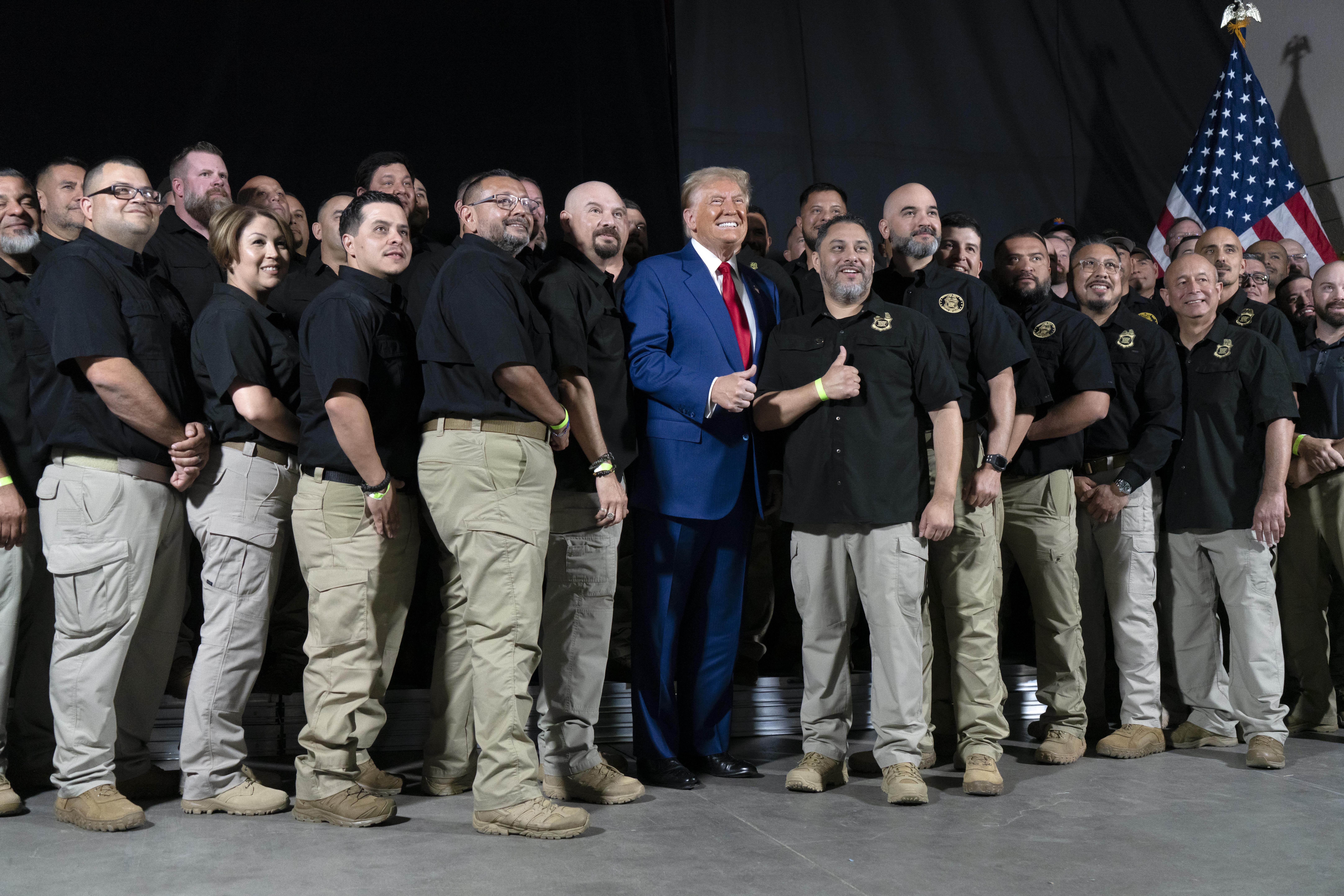 Donald Trump smiles as he is surrounded by Border Patrol agents in polo shirts.