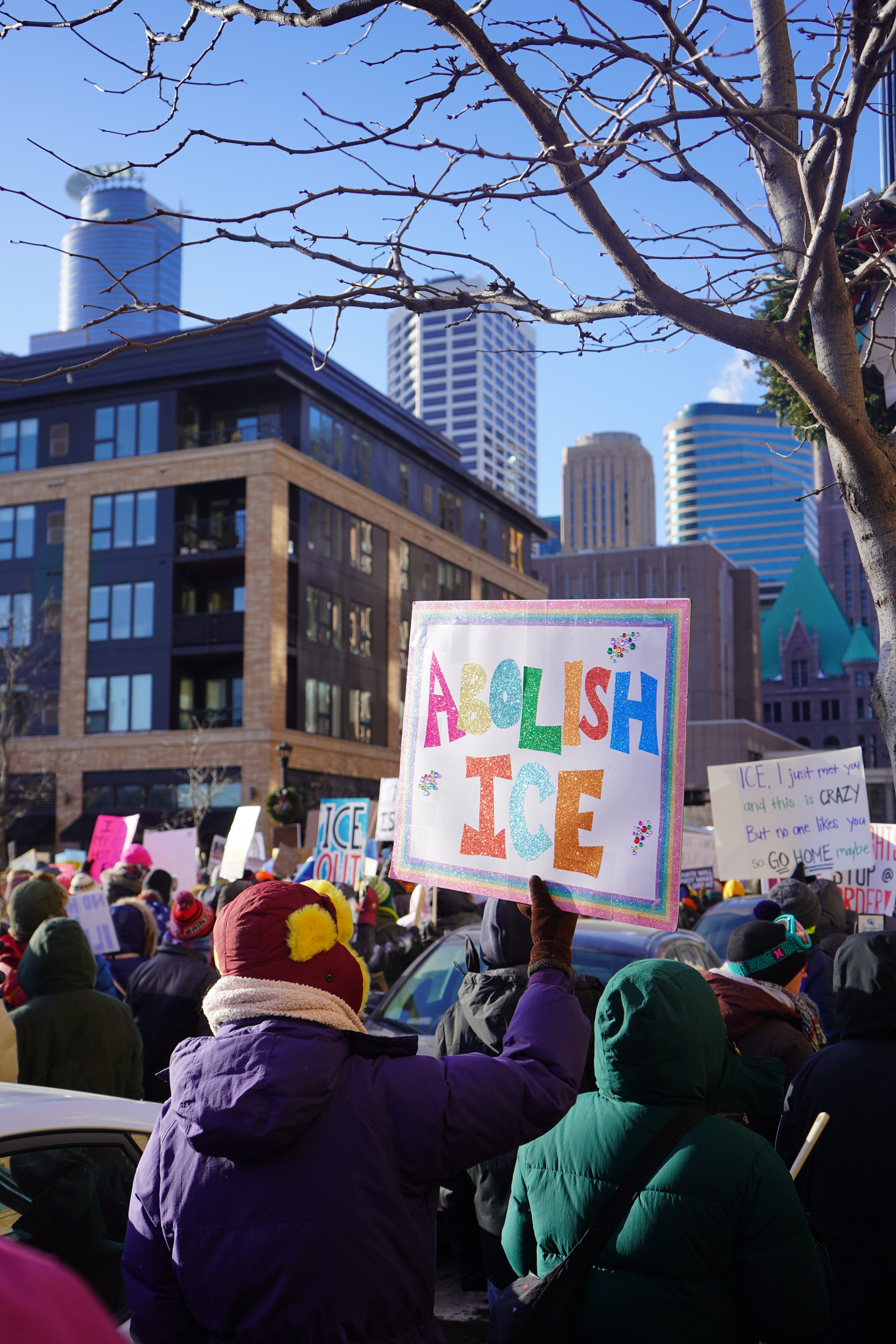 Protestors in winter jackets carrying anti-ICE signs. 